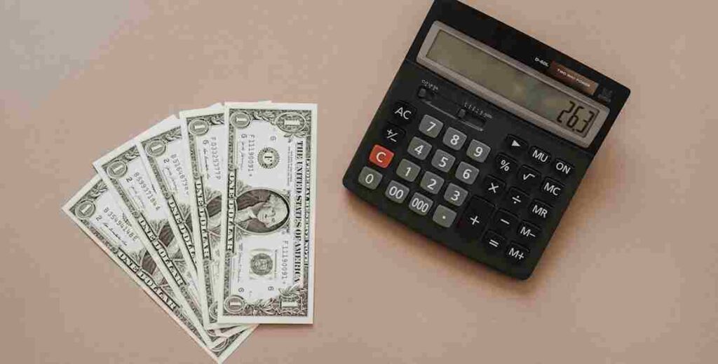 jacobstrend A big black calculator with five US$1 bills stacked together on a light-brown background